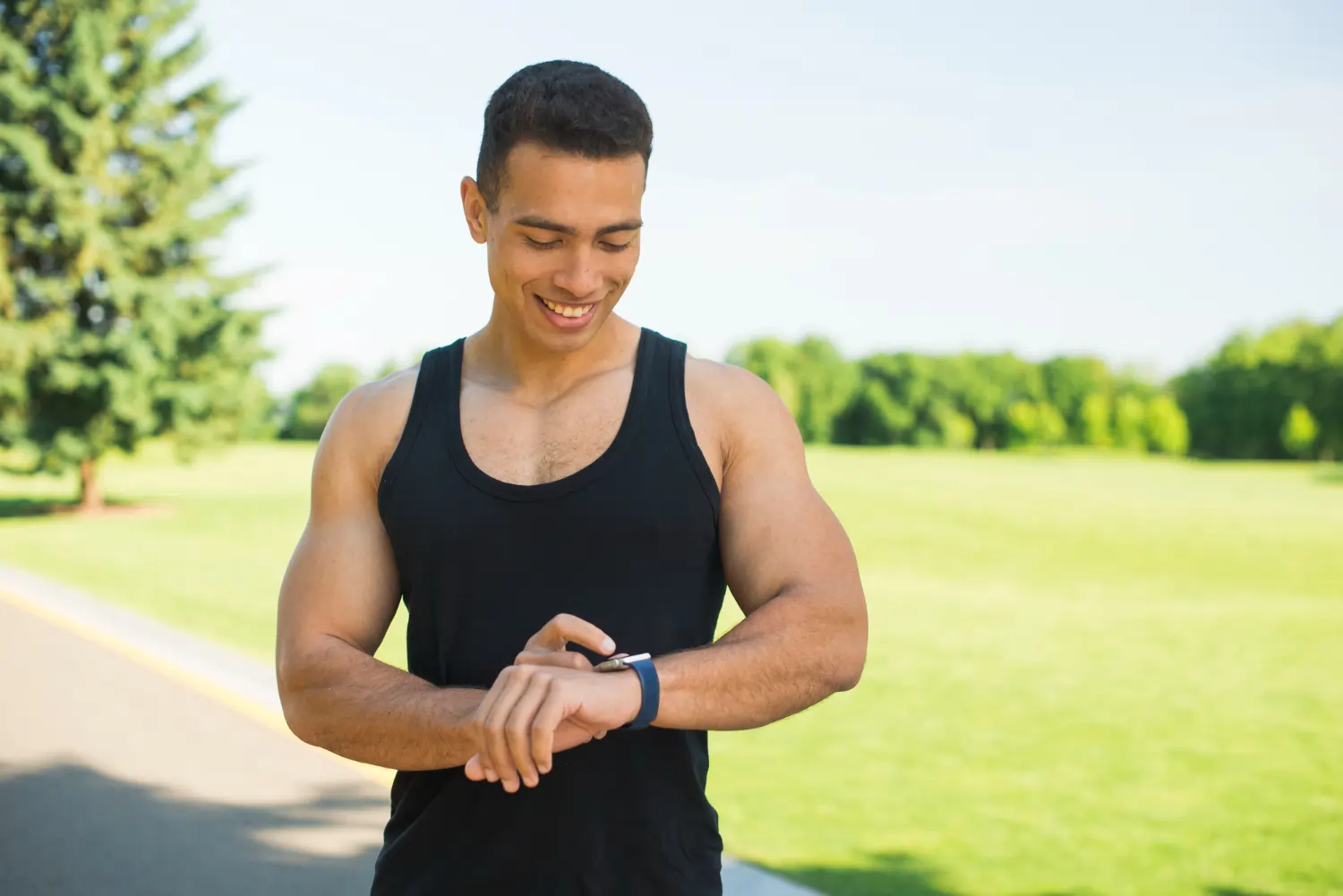 An athletic man checking his smartwatch to determine the best time for workout in an outdoor park.