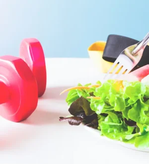Red dumbbells next to a plate of fresh salad and spring rolls, representing workout and diet secrets for weight loss.