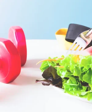 Red dumbbells next to a plate of fresh salad and spring rolls, representing workout and diet secrets for weight loss.