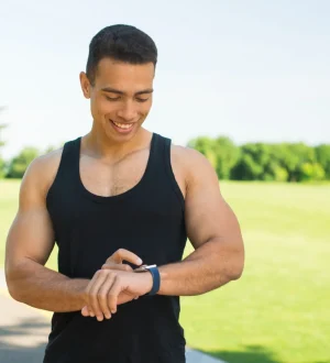 An athletic man checking his smartwatch to determine the best time for workout in an outdoor park.