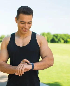 An athletic man checking his smartwatch to determine the best time for workout in an outdoor park.