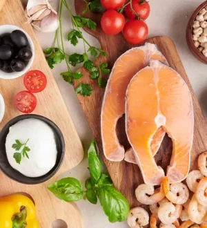 Top view of raw salmon, shrimp, fresh vegetables, olives, nuts, and olive oil representing major Mediterranean diet benefits.