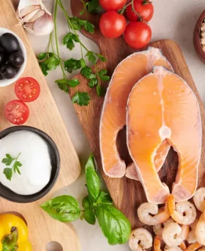 Top view of raw salmon, shrimp, fresh vegetables, olives, nuts, and olive oil representing major Mediterranean diet benefits.