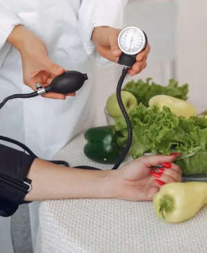 Doctor checking blood pressure beside fresh vegetables for a high blood pressure diet chart pakistan.
