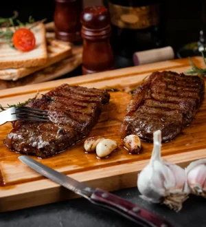 Two pieces of juicy grilled lean beef for weight loss served on a wooden board with fresh garlic and rosemary.