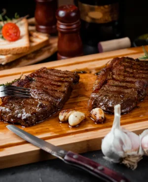Two pieces of juicy grilled lean beef for weight loss served on a wooden board with fresh garlic and rosemary.