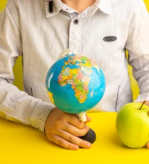 A person holding a small globe in one hand and a fresh green apple in the other over a bright yellow surface, symbolizing global health goals Managing Health Goals Across Time Zones.