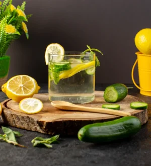 A glass of fresh lemon, cucumber, and mint infused detox water on a wooden platter, recommended as part of a uric acid diet plan in Pakistan.