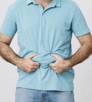 A man pinching lower abdominal fat through a light blue shirt, illustrating stubborn lower belly fat storage.