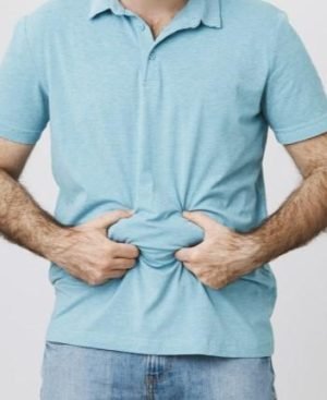 A man pinching lower abdominal fat through a light blue shirt, illustrating stubborn lower belly fat storage.