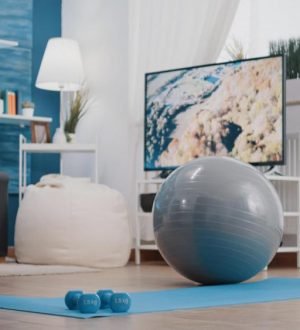 A blue yoga mat with small dumbbells and a grey fitness ball in a living room, showing how to make a gym at home.