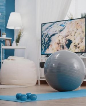 A blue yoga mat with small dumbbells and a grey fitness ball in a living room, showing how to make a gym at home.