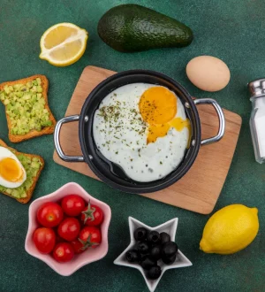 Balanced high-protein breakfast spread with fried egg in a skillet, avocado toast, boiled egg, cherry tomatoes, and fresh lemon for a healthy diet.