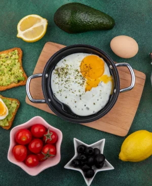 Balanced high-protein breakfast spread with fried egg in a skillet, avocado toast, boiled egg, cherry tomatoes, and fresh lemon for a healthy diet.