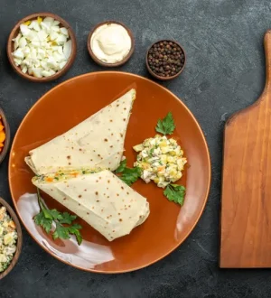 Top-down photo of a healthy PCOS weight loss meal in Pakistan, featuring whole-wheat roti wraps filled with grilled chicken and fresh vegetables, surrounded by healthy nuts, leafy greens, and purple cabbage, on a dark professional surface.