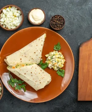 Top-down photo of a healthy PCOS weight loss meal in Pakistan, featuring whole-wheat roti wraps filled with grilled chicken and fresh vegetables, surrounded by healthy nuts, leafy greens, and purple cabbage, on a dark professional surface.